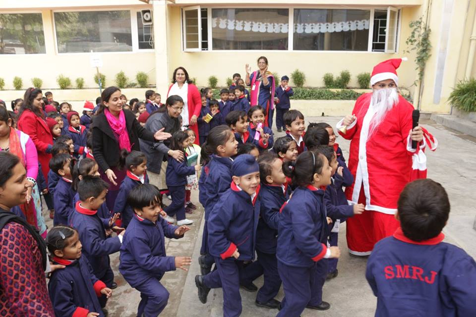 Teacher and children in navy uniforms greet a Santa Claus figure outdoors at a school.