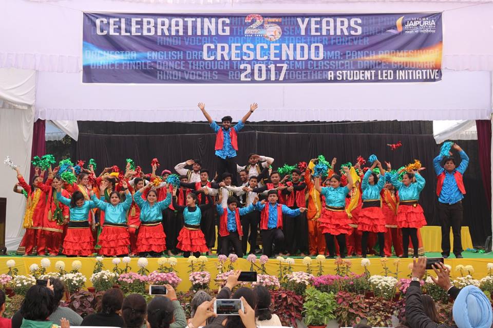 Group of students performing a colorful dance on stage during Crescendo 2017 celebration, audience taking photos in front.