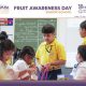 Students in yellow uniforms work together on fruit-themed crafts during Fruit Awareness Day in a classroom setting.