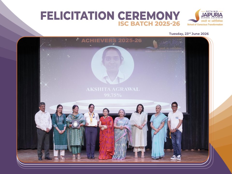 Group of award recipients and staff posing on stage after a felicitation ceremony, some holding certificates and a trophy