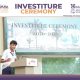 Boy in white shirt speaks at podium during school investiture ceremony; banner behind reads 'Investiture Ceremony 2026-2027' with school logos nearby.