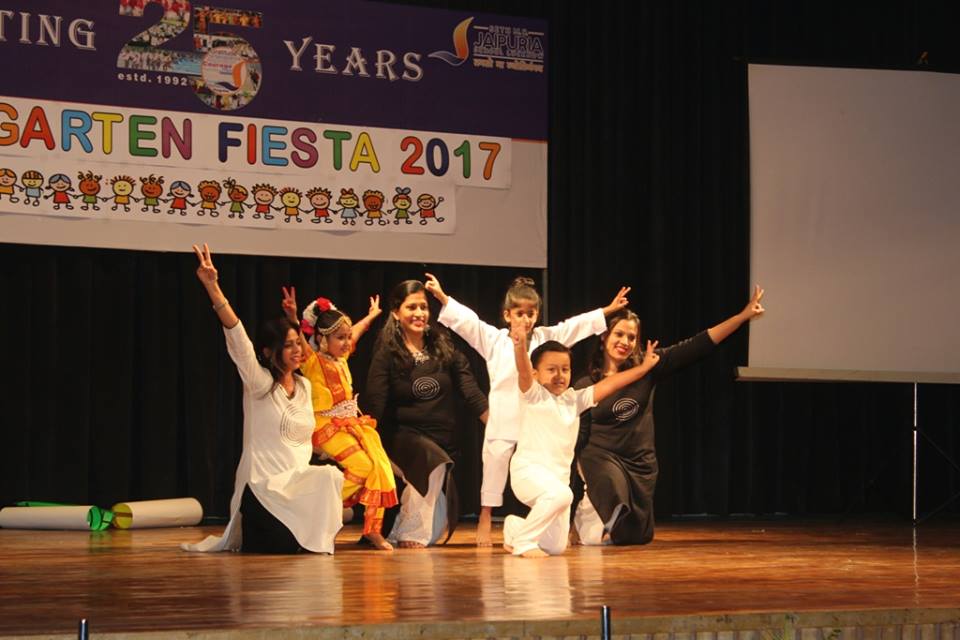 Group of dancers on stage mid-performance, several in white or black outfits, a child in bright yellow, backdrop reads 'GARTEN FIESTA 2017'.