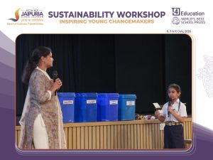 Woman speaks into a microphone on stage beside blue labeled recycling bins at a sustainability workshop.