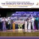 Group of people in formal attire on a stage during an award ceremony, with a large 'WORLD'S TOP 10' display in the background.