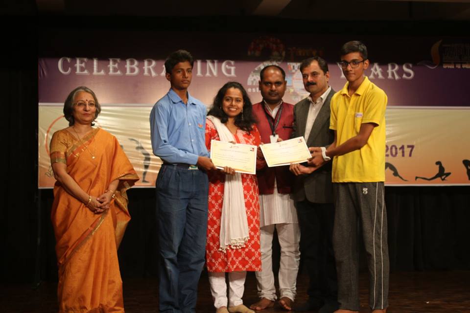 Group of six people on stage presenting certificates at an event, banner behind reads 'CELEBRATING YEARS'.