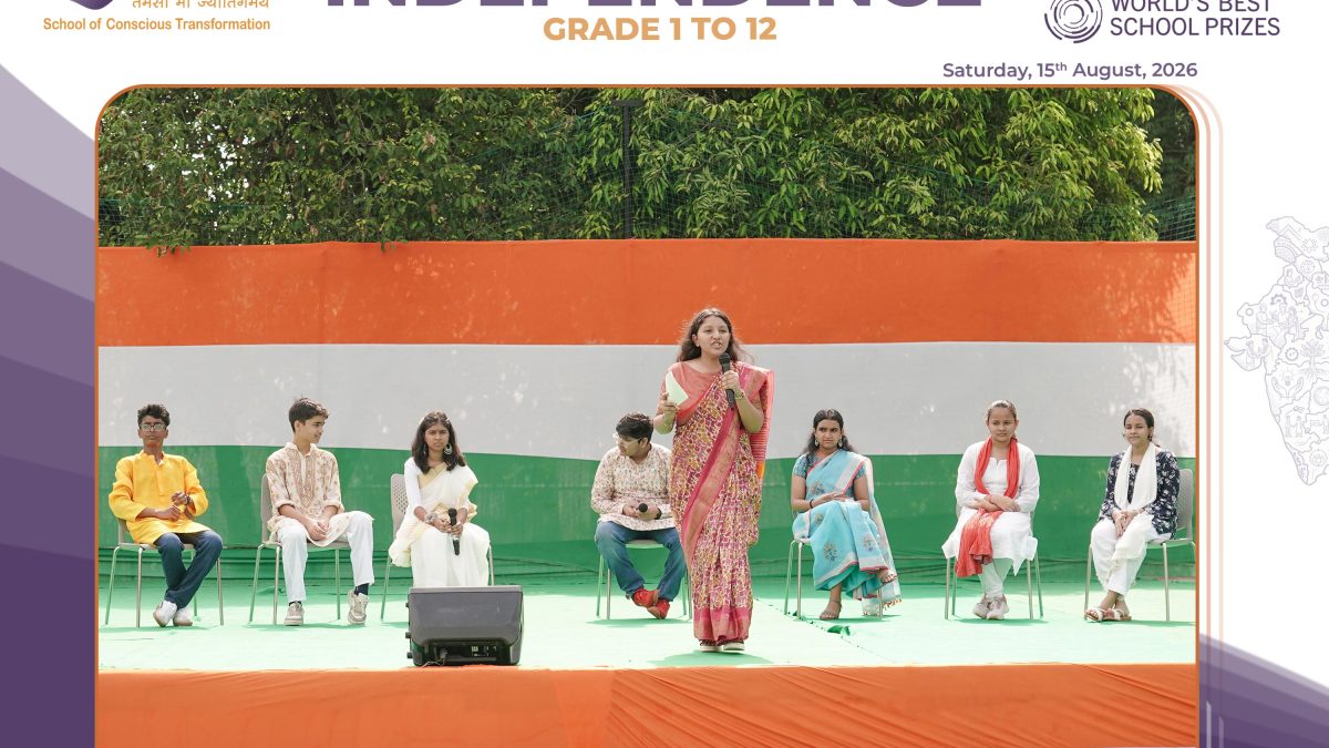 Group of students seated on a green stage as a woman in a saree speaks during a school Independence Day program.