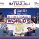 Two people sit in armchairs on a stage during a school event interview, with a blue backdrop and large trophies behind them, and a banner reading 'Seth M.R. Jaipuria School Lucknow' visible above.