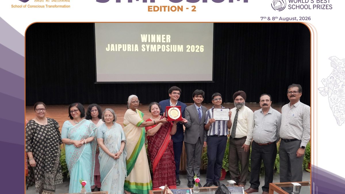 Group of award recipients and attendees posing on stage at Jaipuria Symposium 2026 winner ceremony on screen behind them.