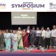 Group of award recipients and attendees posing on stage at Jaipuria Symposium 2026 winner ceremony on screen behind them.