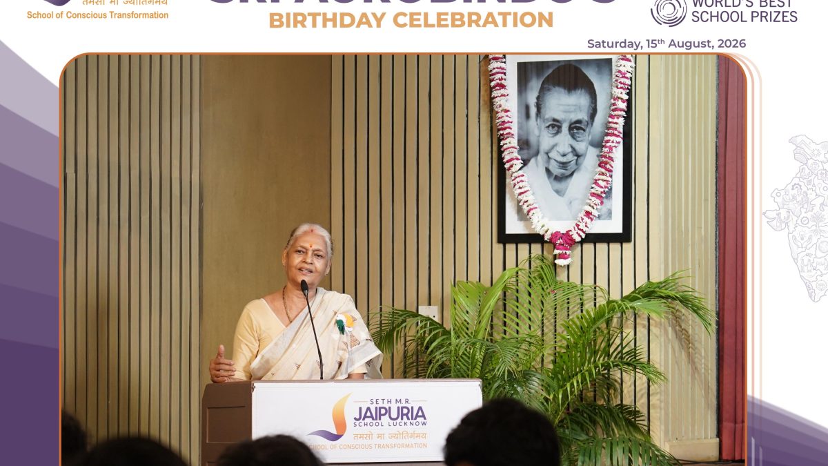 Woman speaking at a podium during a celebration event, with a banner reading 'Seth M.R. Jaipuria School Lucknow' in the background.