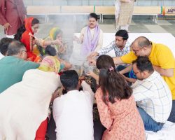 Group of people in traditional Indian attire seated in a circle around a small fire pit, performing a ritual together.