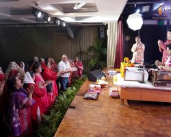 Audience of women in bright red and pink traditional outfits watching a stage ceremony.