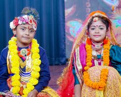 Two children in vibrant traditional Indian costumes with floral garlands posing on a stage.