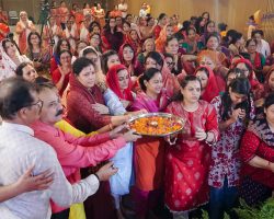 Crowd of Indian women in colorful sarees at a ceremony, with a man holding a tray of marigold petals in the foreground