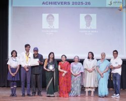 Group of students and teachers on a stage during an awards ceremony; one student holds a certificate and another a trophy.