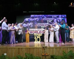 Group of people on a stage during an award ceremony, clapping as a large screen shows 'WORLD'S TOP 10' in the background.