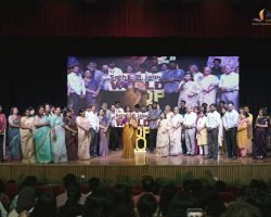 Group photo of many people in formal attire on a stage during a school event, with a banner and backdrop behind them.