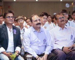 Group of attendees in a conference audience, wearing white shirts and badges, focused on the event.