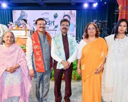 Five adults in traditional Indian attire posing for a photo on a decorated stage at a cultural event.